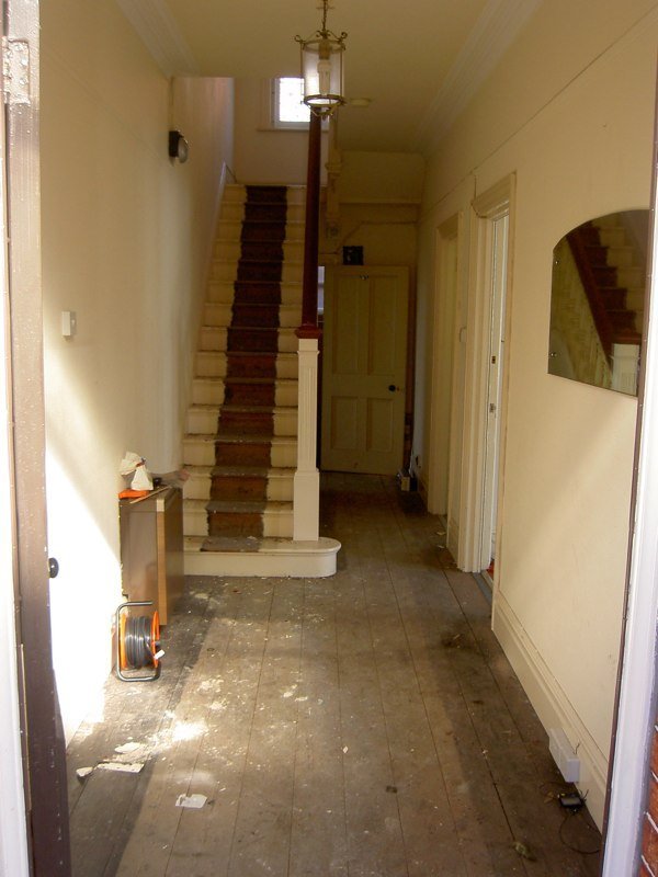 The same hallway, stripped back to bare floorboards and plaster